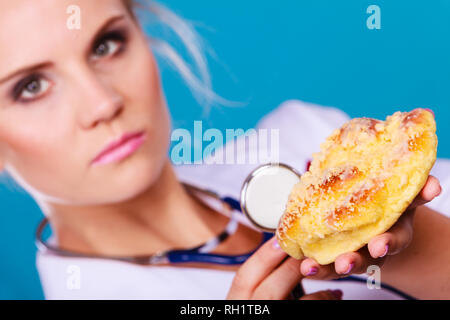 Serious dietitian nutritionist checking examine sweet roll bun with stethoscope. Woman with fattening junk food. Bad unhealthy eating nutrition concep Stock Photo