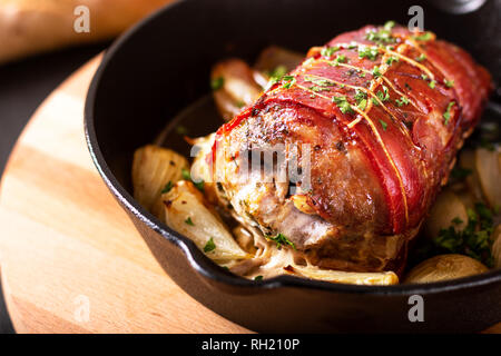 Food concept homemade Bacon Stuffed Pork Tenderloin baked in iron cast skillet on round wooden board Stock Photo