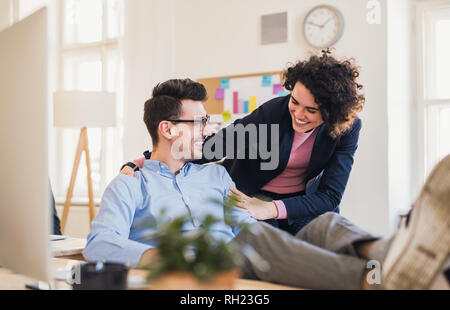 Two young cheerful businesspeople working together in a modern office, feet on a desk. Stock Photo