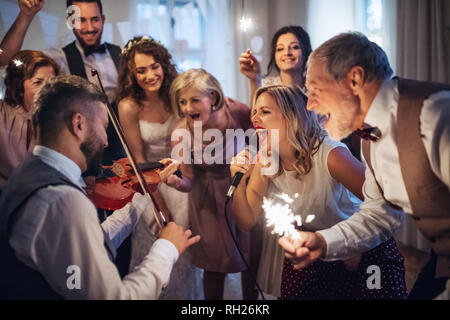 A young cheerful bride, groom and other guests dancing, singing and playing violin on a wedding reception. Stock Photo