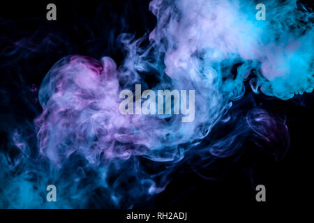 Dense exhaled blue purple and white smoke in the form of a cloud on a black background moves smoothly into the dissolving vapor column from the vape.  Stock Photo