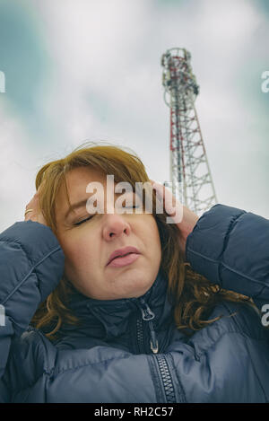 The woman is holding her head near the BTS. Harmful radiation from cellular network transmitters concept Stock Photo