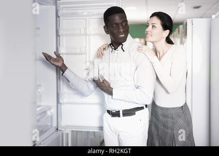 Interracial couple choosing fridge in store of household appliances Stock Photo
