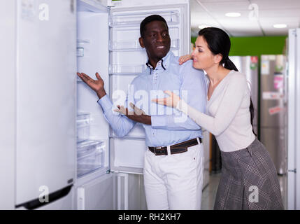 Interracial young couple choosing fridge in store of household appliances Stock Photo