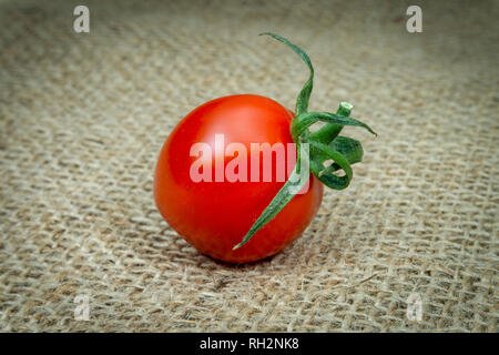Single fresh red cherry tomato on burlap canvas background Stock Photo