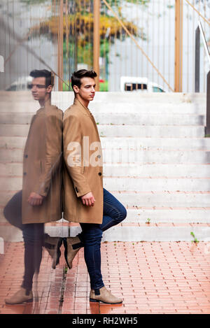Side view of young stylish man leaning on black wall while looking away outdoors in sunny day Stock Photo