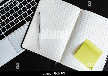 blank open note pad with yellow sticky note next to laptop computer Stock Photo
