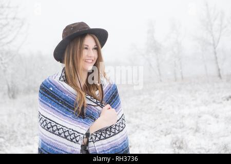 young woman in the snow wearing a bohemian style blanket and hat during a winter storm. Stock Photo