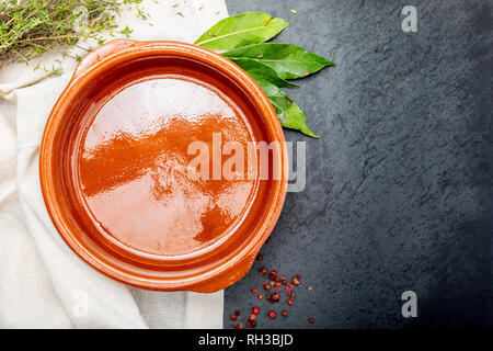 Empty clay pot with pepper, bay leaf and thyme. On black background. Concept to include your food and your text. Stock Photo