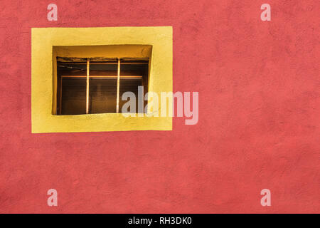 Minimalist wall design of a textured red wall with a yellow window from in upper  left,  Window has no glass, but checkered bars. Stock Photo
