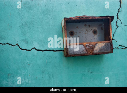 Teal textured wall, with long traversing crack and a rusted metal mailbox Stock Photo