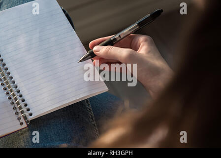 Woman seated with open notebook in lap and holding pen in hand Stock Photo