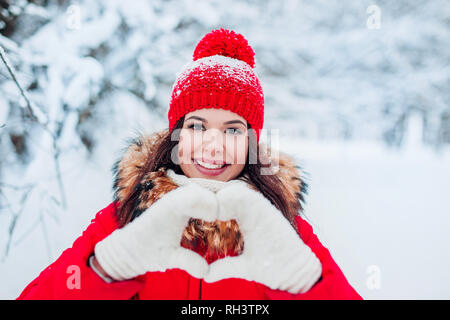 Pretty romantic young woman making a heart gesture with her fingers in front of her chest showing her love on winter background Stock Photo
