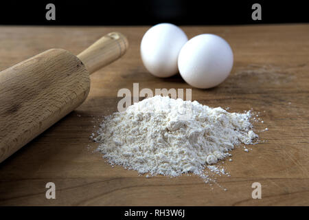 A concept photo of flour in a pile, two eggs, and a rolling pin. Stock Photo