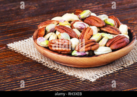 Nuts mix in a wooden plate over wooden background(selective focus). Stock Photo