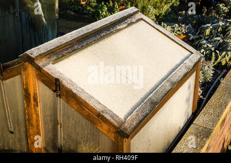 A frost-covered wooden cold frame on a raised bed protecting plants during January in an English garden Stock Photo