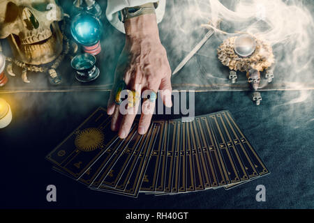 Hand of fortune teller and tarot card on the table under candlelight. Dark tone. Stock Photo