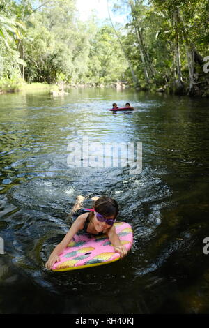 Young girl paddles on a boogie board with family in background, Finch Hatton, Queensland 4756, Australia