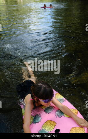 Young girl paddles on a boogie board with family in background, Finch Hatton, Queensland 4756, Australia