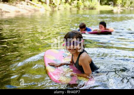 Young girl paddles on a boogie board with family in background, Finch Hatton, Queensland 4756, Australia