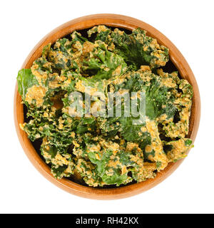 Homemade kale chips in wooden bowl. Dehydrated green leaf cabbage, coated with blended spices, nuts and vegetables. Snack and potato chip substitute. Stock Photo