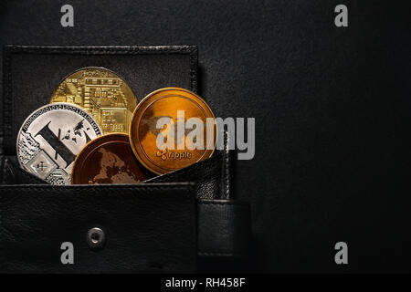 Wallet full of shinning coins of cryptocurrency (golden bitcoin, litecoin, ripple) on black and dark background. Stack of crypto coins saved in wallet. Stock Photo