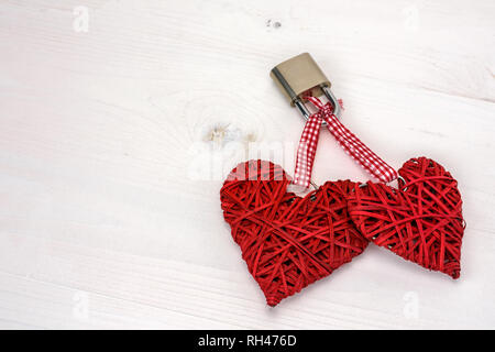 Two red hearts locked with a padlock on a white wooden background. Valentines day card concept. Stock Photo