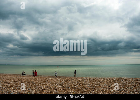 A few distant figures watch on a pebbly beach as an ominous and threatening storm is brewing over the sea, heading towards them. Stock Photo