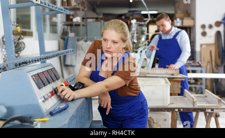 Experienced female worker of glass factory engaged in adjustment of glass chamfering machine Stock Photo