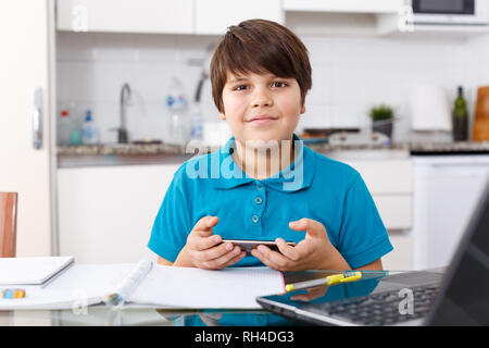 Portrait of boy doing homework and using mobile phone in kitchen at home Stock Photo
