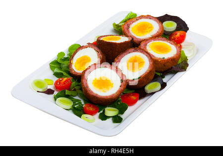 Traditional British picnic food - delicious Scotch eggs cut in halves with vegetable salad of greens and tomatoes. Isolated over white background Stock Photo