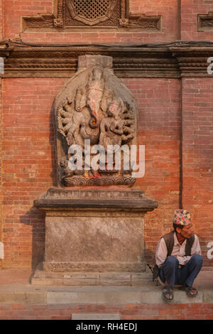 A man sitting next to a sculpture of elephant god Ganesha, at Patan Royal Palace, Durbar Square, Patan (Lalitpur), Kathmandu Valley, Nepal Stock Photo