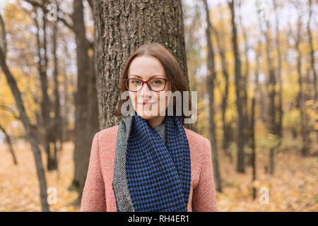 Portrait confident woman in scarf standing against tree in autumn park Stock Photo