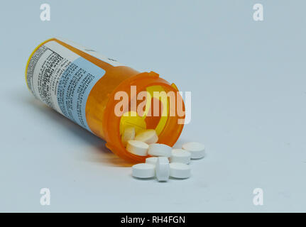 Prescription pain pills are spilling out of the plastic pill container which is laying on its side. Stock Photo