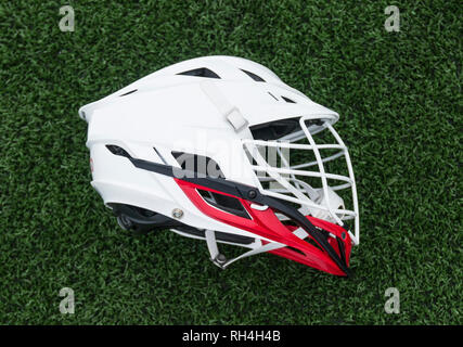 A red and white lacrosse helmet is laying on its side on a green turf field. Stock Photo