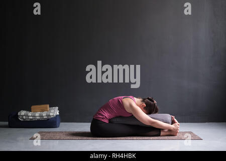woman practicing yoga, doing Seated forward bend pose, using bolster. Stock Photo