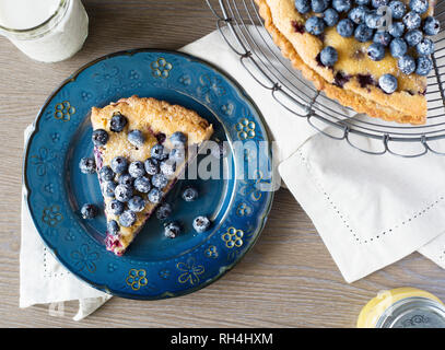 overhead view of blueberry lemon pie on antique blue plate with cake stand, milk, and napkin. Stock Photo