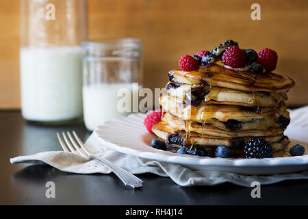 stack of pancakes on white antique plate with syrup and mixed berries and milk in mason jar. Stock Photo