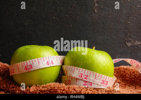 HEALTH LIFESTYLE CONCEPT: Green apples and measuring tape over black rustic background. Selective focus. Stock Photo