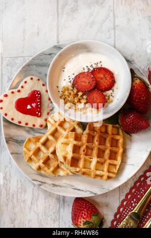 Valentines day breakfast heart shaped waffles yogurt granola bowl fresh strawberries, overhead view Stock Photo