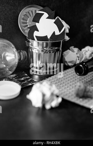 trash can with recycle symbol surrounded by reusable waste materials like plastic paper and glass, concept of reducing damage to the environment Stock Photo