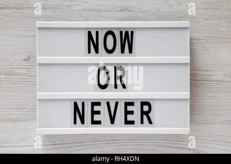 'Now or never' word on modern board on a white wooden surface, top view. From above, flat lay, overhead. Stock Photo