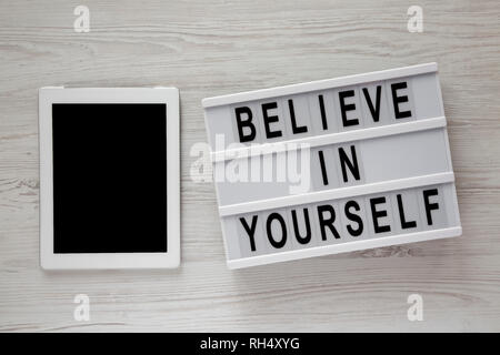 Lightbox with text 'Believe in yourself', tablet on a white wooden background, top view. From above, flat lay, overhead. Stock Photo