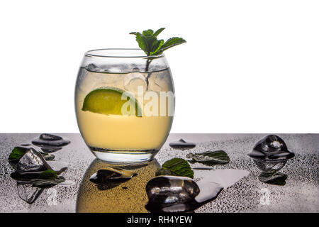 A mojito cocktail in a small oval glass garnished with mint and lime on a glossy base and back lit background Stock Photo