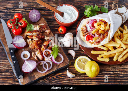 overhead view of greek souvlaki, pita ma gyros with chicken meat, vegetables, french fries and yogurt garlic sauce, ingredients on a cutting board on  Stock Photo