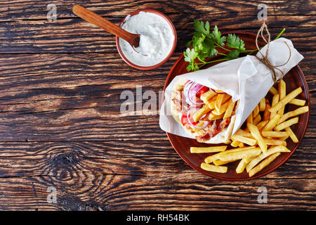 overhead view of greek souvlaki, pita ma gyros with chicken meat, vegetables, french fries on a earthenware plate and tzatziki sauce in a bowl on a ru Stock Photo