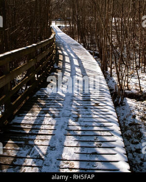 A wooden walkway in Frick Park, Pittsburgh, Pennsylvania, USA covered in snow with the railing casting shadows Stock Photo