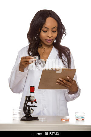 Black female scientist wearing a lab coat with microscope and petri dish doing micro biology research.  She is working in the education or medical ind Stock Photo