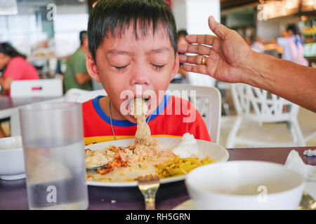 Boy puking on plate after having lunch meal in food court with helping hand Stock Photo