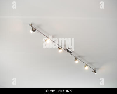 Modern stainless steel track light hanging on white ceiling background. Stock Photo